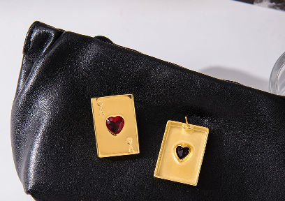 Brinco Ás de Copas dourado com coração vermelho usado na orelha mostrando tamanho e proporção da peça.