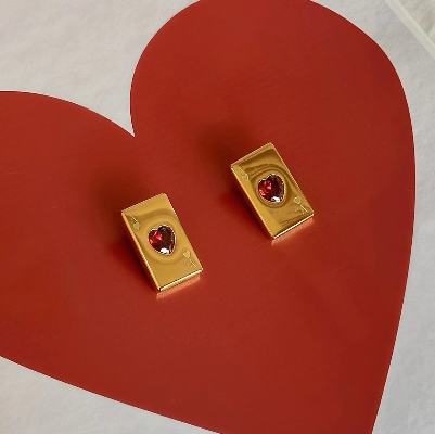 Brinco Ás de Copas dourado com coração vermelho usado na orelha mostrando tamanho e proporção da peça.